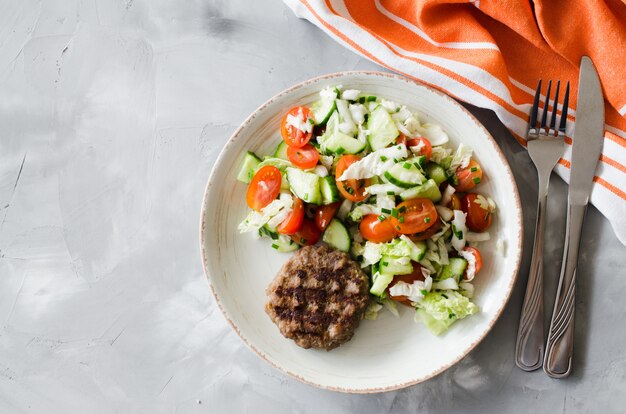 Sappige geroosterde kotelet met verse groentesalade op grijze achtergrond.