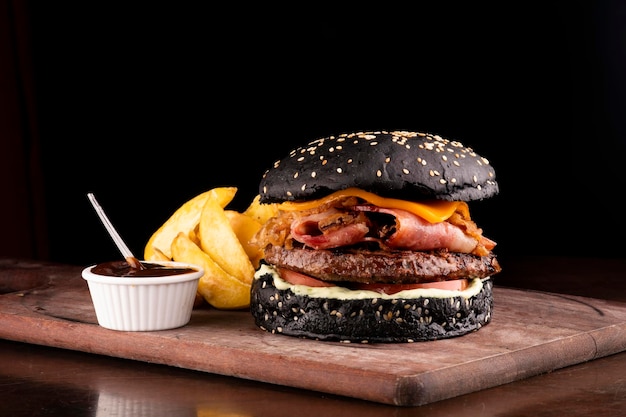 Sappige grappige hamburger met halloween-thema, knapperige zwarte gebrande bacon en uienplakken met sesam op een houten bord met rustieke frietcombo