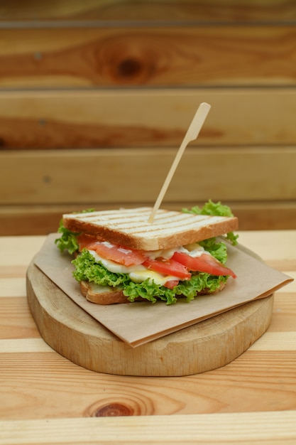 Sappige sandwich met spek, verse groenten, groene salade en donkere lijnen na grill op houten plaat