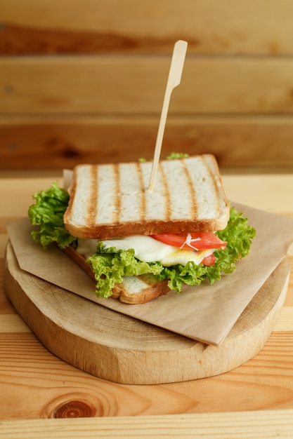 Sappige sandwich met spek, verse groenten, groene salade en donkere lijnen na grill op houten plaat