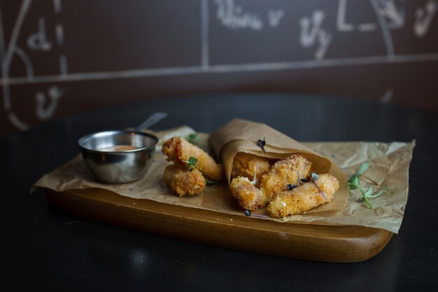 Sappige smakelijk gebakken kipnuggets in kaas gepaneerd met kaassaus versierd met Groenen op een houten bord in een restaurant. Snel lekker eten. Mooie portie eten. Zelfgemaakt eten