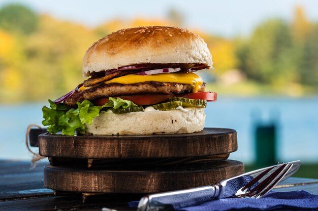 Sappige smakelijke cheeseburger met rundvlees, sla, augurken, tomaat en uienringen op een houten tafel. Klassiek straatvoedsel - gegrilde hamburger