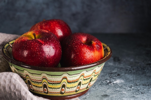 Sappige verse rode appels met waterdruppels in geschilderde kom op keukenhanddoek op grijze achtergrond