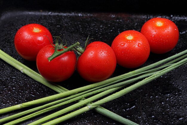 Sappige zoete rode tomaten en groene takjes op een zwarte achtergrond Gezonde voeding concept close-up