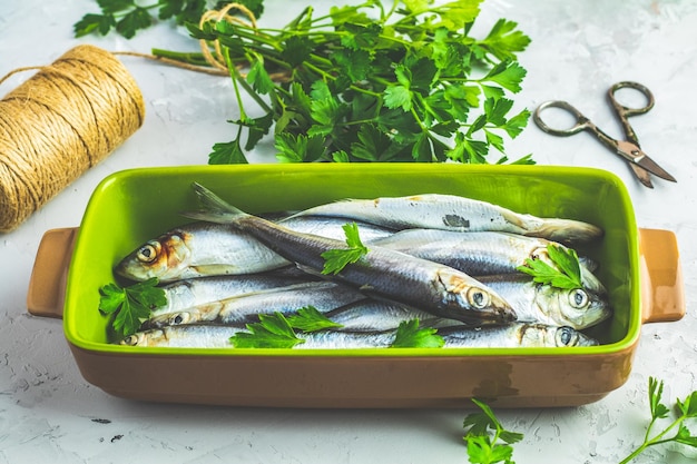 Сардины или балтийская сельдь на зеленом блюде с петрушкой на светло-серой бетонной поверхности стола Сырая сырая морская рыба