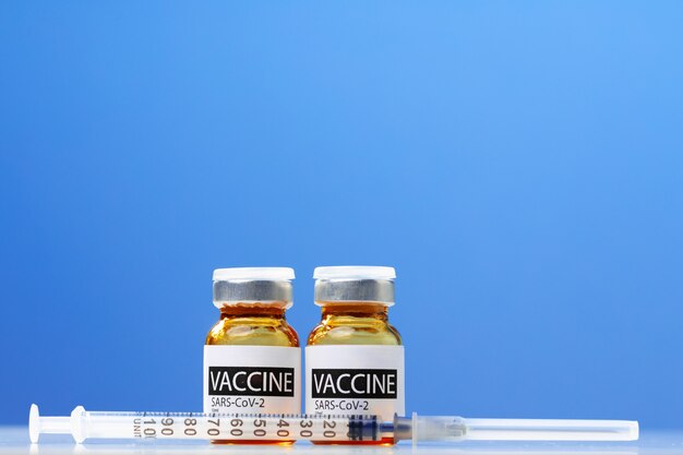 白いテーブルの上のSars-cov-2ワクチンバイアルと注射器