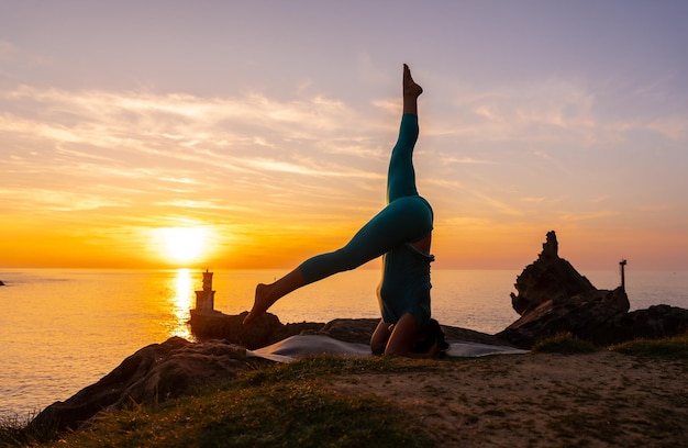 Sarvangasana una donna che fa esercizi di meditazione e yoga su una roccia al tramonto accanto a un faro nel mare vita sana e naturista