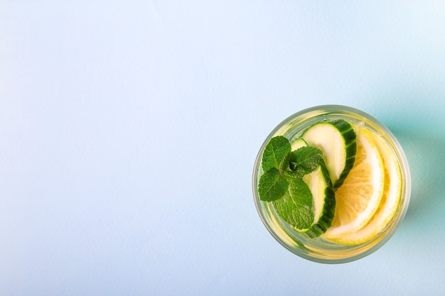 Sassy water for detox infused with lemon, cucumber and mint in glass on light blue background. Top view. Healthy lifestyle concept. Space for text.