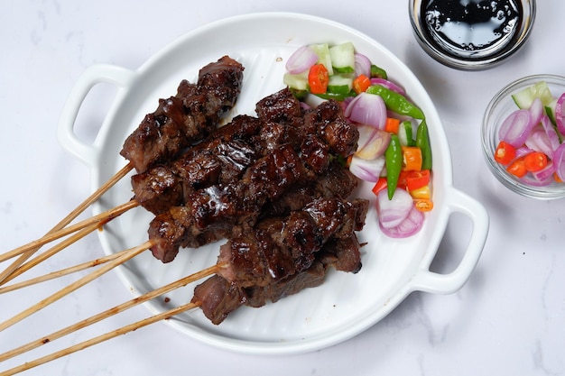 Photo satay or sate skewered and grilled meat, served with spicy salad ,cucumber,chili and soy sauce,