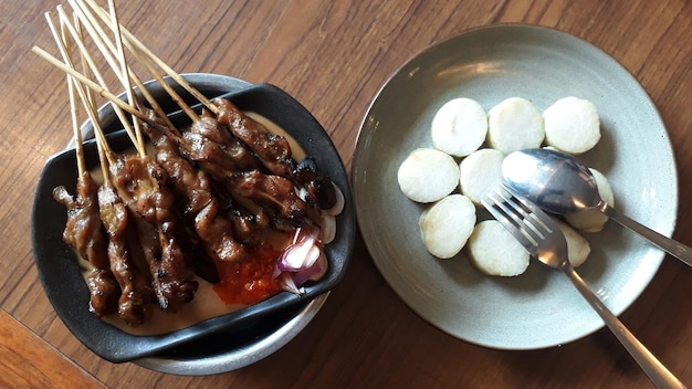 Sate Ayam of Chicken Satay geserveerd op hete plaat met een bord Lontong of rijstwafels