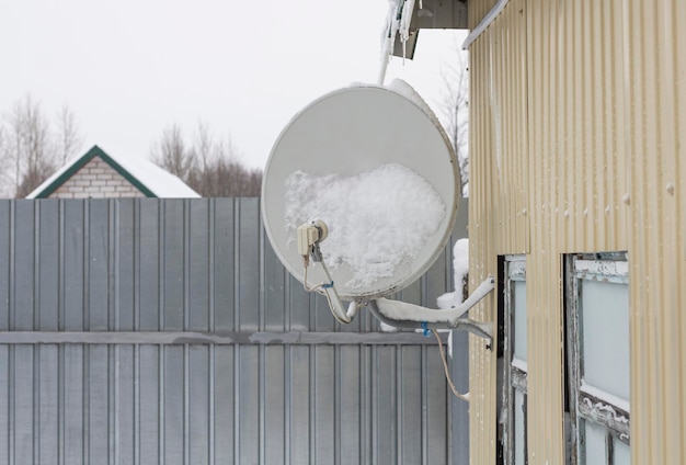 Satellietschotel bevestigd aan de muur van een huis in de sneeuw na een sneeuwval