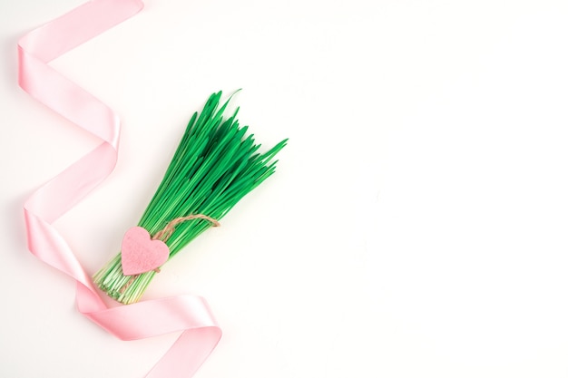 Satin pink ribbon bouquet with a heart on white background. Top view