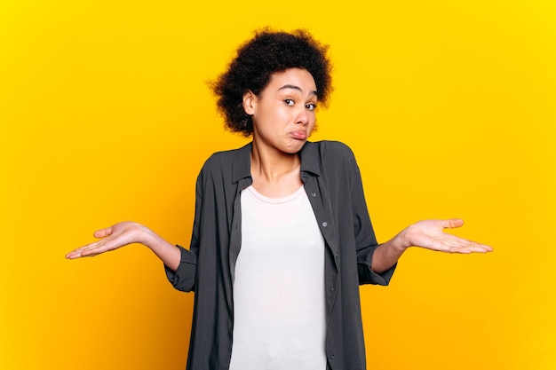 Photo satisfied african american or brazilian lovely curly haired woman in casual wear points with hand to the side at empty space for advertise smile at camera stand on isolated orange background
