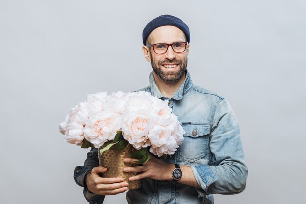 Satisfied bearded male with cheerful expression has broad smile, holds bunch of flowers