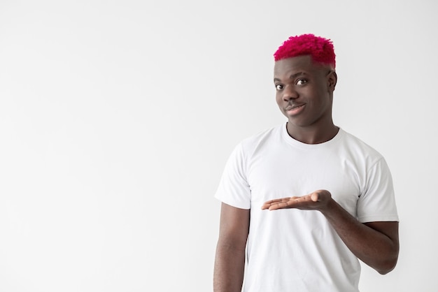 만족한 흑인 남성 광고 제품 판촉 활동 좋은 제안 큰 판매 밝은 분홍색 머리 흰색 티셔츠를 입은 웃고 있는 아프리카 남자 복사 공간을 보여주는 열린 손바닥 고립된 빛