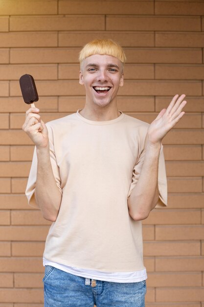 Satisfied blond Caucasian guy holding an ice cream stick in hand looking at the camera