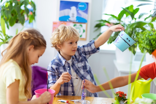 満足した少年。エコロジーレッスンでクラスメートと植木鉢を描いた後、満足しているブロンドの髪の少年