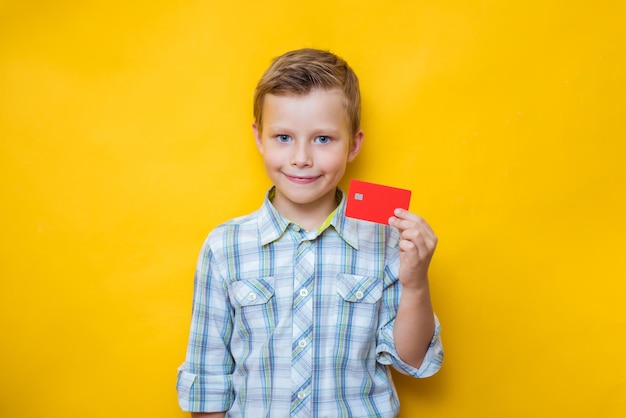 Satisfied boy holding a credit bank card isolated on yellow color wall background child studio