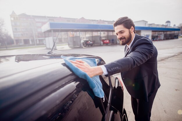 Satisfied businessman polishing his expensive car in front of car wash.