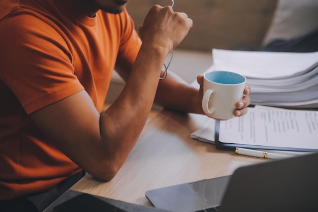 Satisfied caucasian successful guy freelancer or ceo relaxes at workplace with legs thrown on table Stylish guy uses laptop browses the Internet looks for ideas for a project sitting at the desk