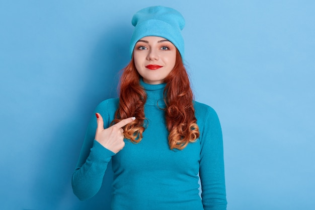 Satisfied Caucasian woman with red hair points at herself