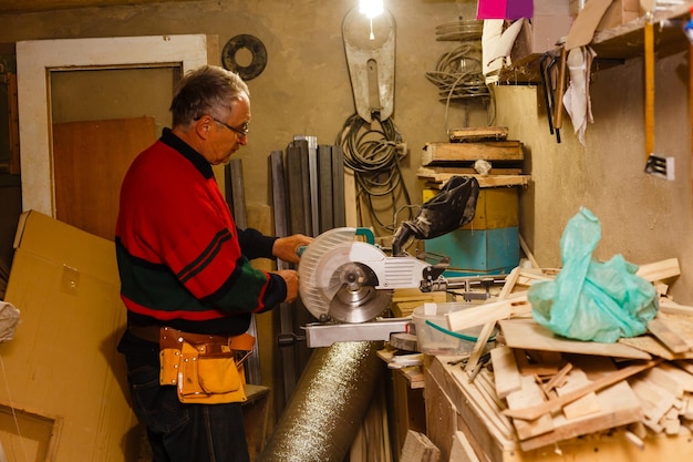 Satisfied cheerful joyful smiling woodmaster is standing near desktop in his workshop, workstation