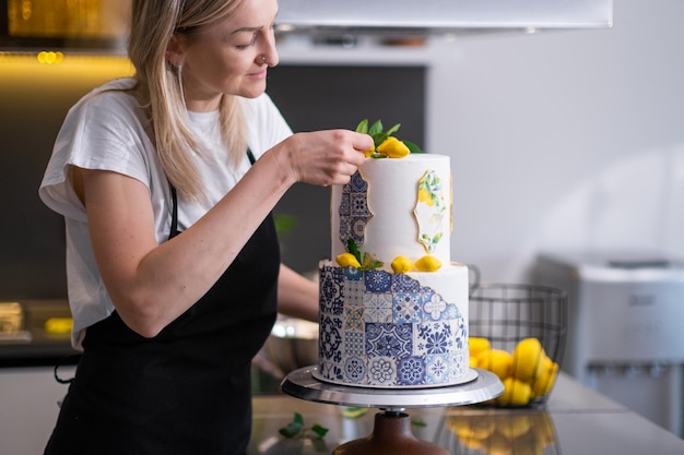 Photo satisfied confectioner in apron decorating twotiered cake with patterns and yellow lemons