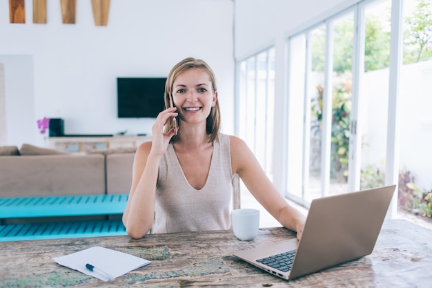 Satisfied female speaking on phone while browsing laptop