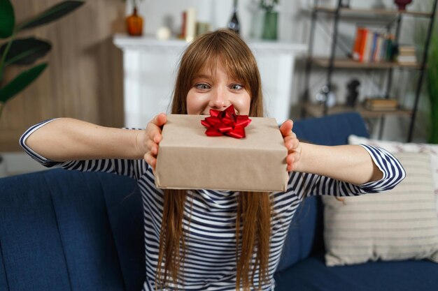 Foto una ragazza soddisfatta guarda con ammirazione una scatola regalo mentre è seduta sul divano all'interno