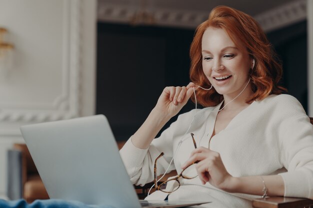 Satisfied happy foxy successful woman has video conference, uses modern laptop computer