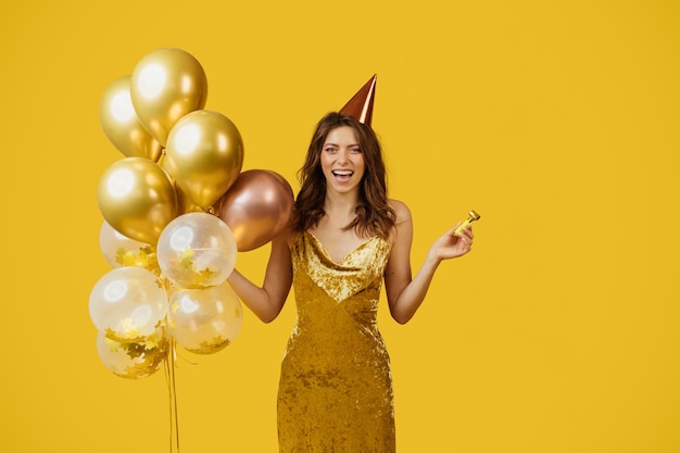 Satisfied lady in dress with balloons birthday cap and party blower celebrating special occasion