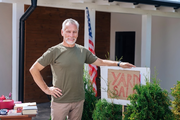 Satisfied man. Bearded beaming man wearing dark khaki shirt feeling satisfied after organizing amazing yard sale