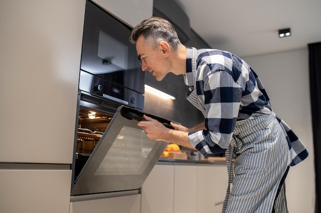 Photo satisfied man opening looking into oven