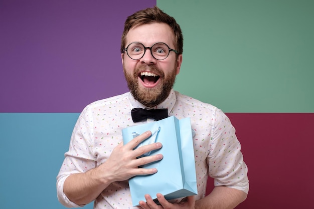 Photo satisfied man received a pleasant surprise is happy joyfully presses a bag with gift to chest