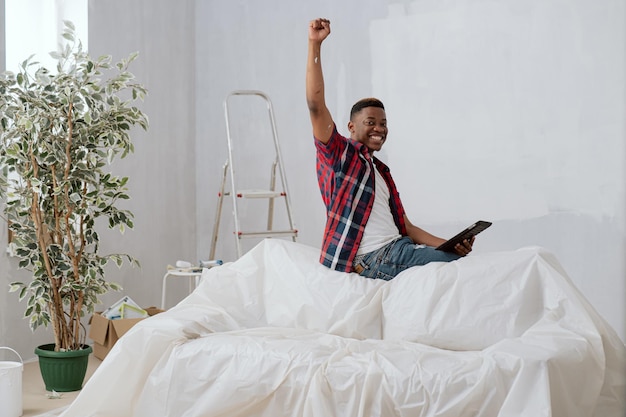 Satisfied man with dark complexion is sitting on backrest of couch