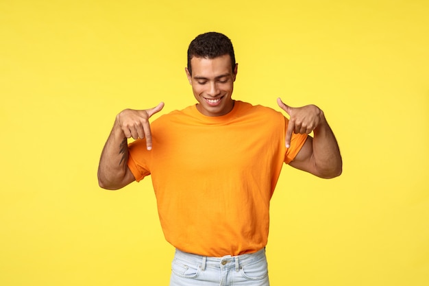 Satisfied masculine guy with short dark haircut,  pointing and looking down