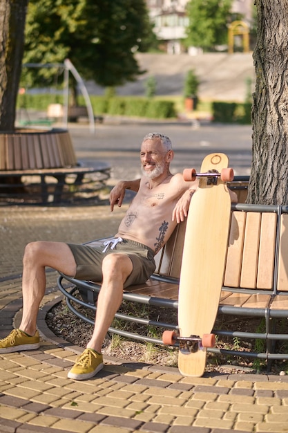 都市公園のベンチに座っているロングボードで満足した成熟した男性