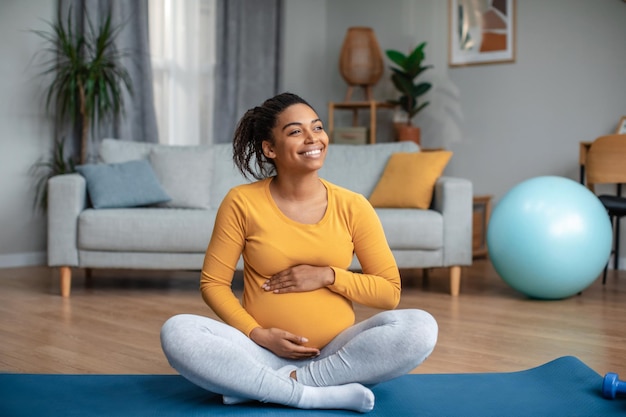 Satisfied millennial pregnant african american lady touching big belly feels movement of baby practicing yoga