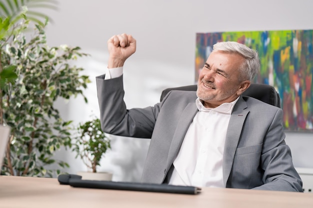 Satisfied old guy dressed in suit sits in front of computer
received good news money in bank