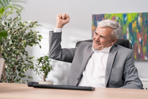 Photo satisfied old guy dressed in suit sits in front of computer received good news