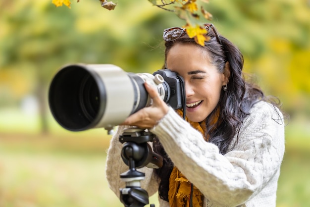 A satisfied photographer is standing behind her camera placed on a tripod taking autumn photos