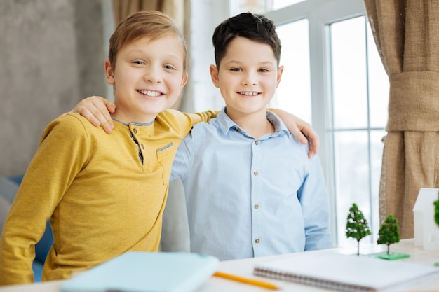 Satisfied with results. Joyful pre-teen boys hugging each other and posing for the camera, smiling brightly, having finished the work on their ecology project