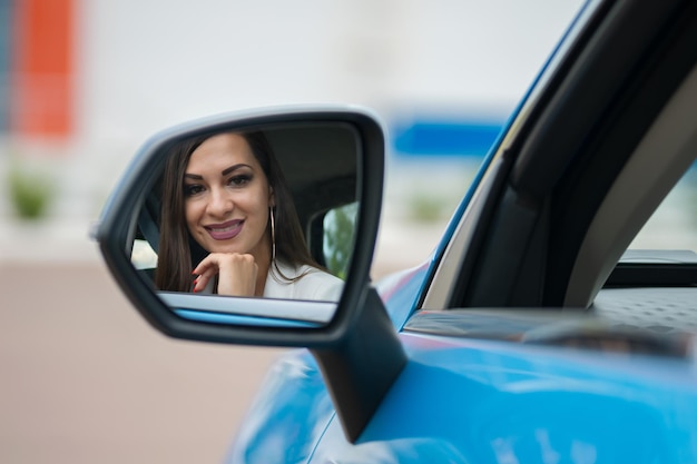 Satisfied woman looks at own reflection in rear view mirror