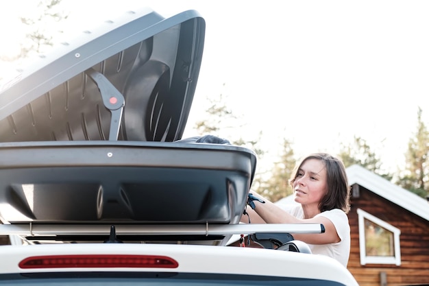 Photo satisfied woman puts things in roof rack of car or in cargo box before a family trip on vacation