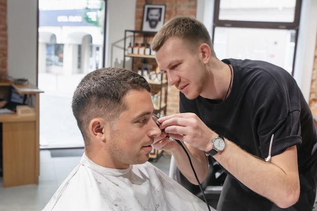 Satisfied young caucasian man doing hairstyle in barbershop.