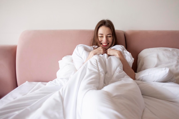 満足した若いかわいい女性は朝、毛布の下でベッドに横たわります。女性は快適なベッドリネンで目覚めます。