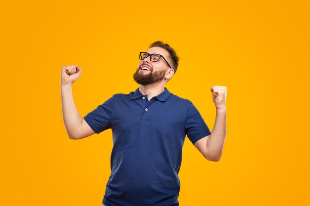 Satisfied young guy with clenched fists celebrating victory in yellow studio