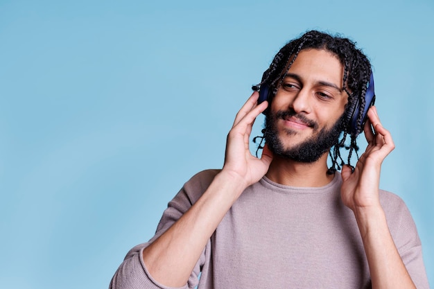 Satisfied young man listening to music while checking sound in new headphones. Arab person with pleasant facial expression enjoying song in wireless earphones and looking away