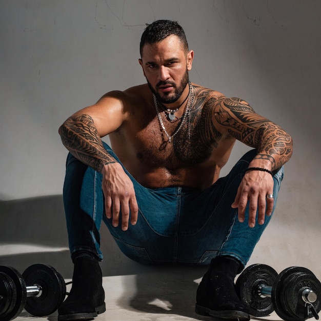 Satisfied young strength man lifting dumbbells shirtless bodybuilder is doing exercise with dumbbell