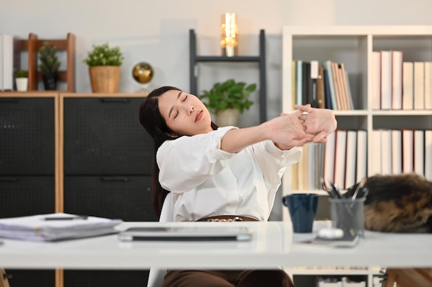 Foto giovane donna soddisfatta che allunga le braccia prendendo una pausa dal lavoro in una comoda sedia nel moderno ufficio domestico